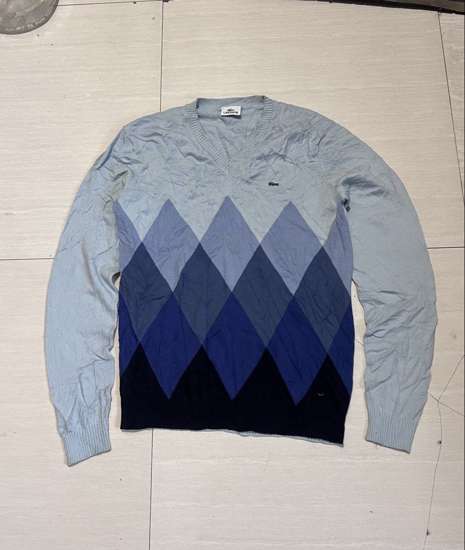 Lacoste Argyle V-Neck Sweater Blue Size 5 (Category: Longsleeves) located in Zamboanga. Submitted by safe.haimer (Listing ID 1469684862, Image 1). Description: - Brand: Lacoste - Design: Blue argyle gradient pattern (light blue to dark navy) - Material: 100% wool - Size: Tagged Size 5 (fits Korean Size 105 / XL) - Features: V-neck, long sleeves, ribbed cuffs and hem - Condition: Excellent, clean inner label and intact tags.