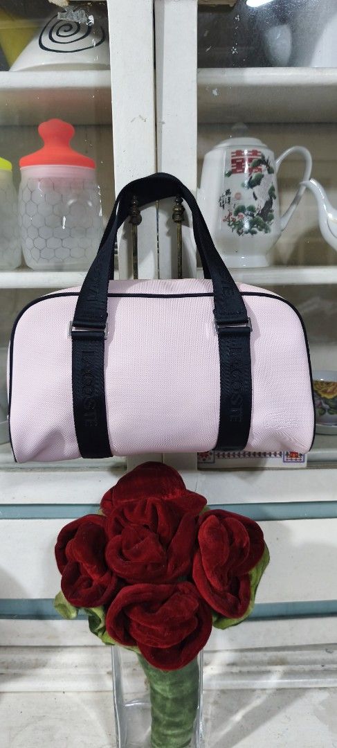 Lacoste Pink Barrel Bag Duffel Bag (Category: Luxury Bags & Wallets) located in Manila. Submitted by shawn0320_fish (Listing ID 1469624417, Image 2). Description: - Brand: Lacoste - Style: Barrel bag - Color: Pink with black accents - Straps: Black woven straps with bold LACOSTE lettering - Closure: Smooth top zipper with contrasting stitching - Structure: Structured design with black piping details - Size: Approximately 11 inches across.