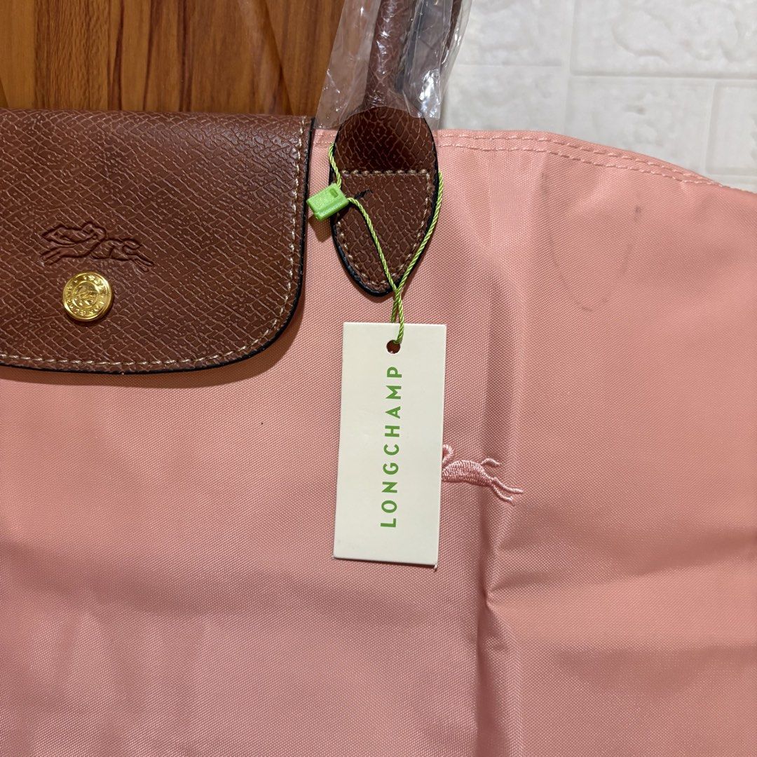 Longchamp Le Pliage Tote Bag (Category: Tote Bags) located in Carmen. Submitted by rr_thrifts (Listing ID 1469688239, Image 3). Description: - Longchamp Le Pliage tote in a charming pink nylon shade - Accented with classic brown leather flap, handles, and gold-tone hardware - Features secure zipper pull and snap button closure - Comes with hanging paper tag attached, perfect for gifting or personal use.