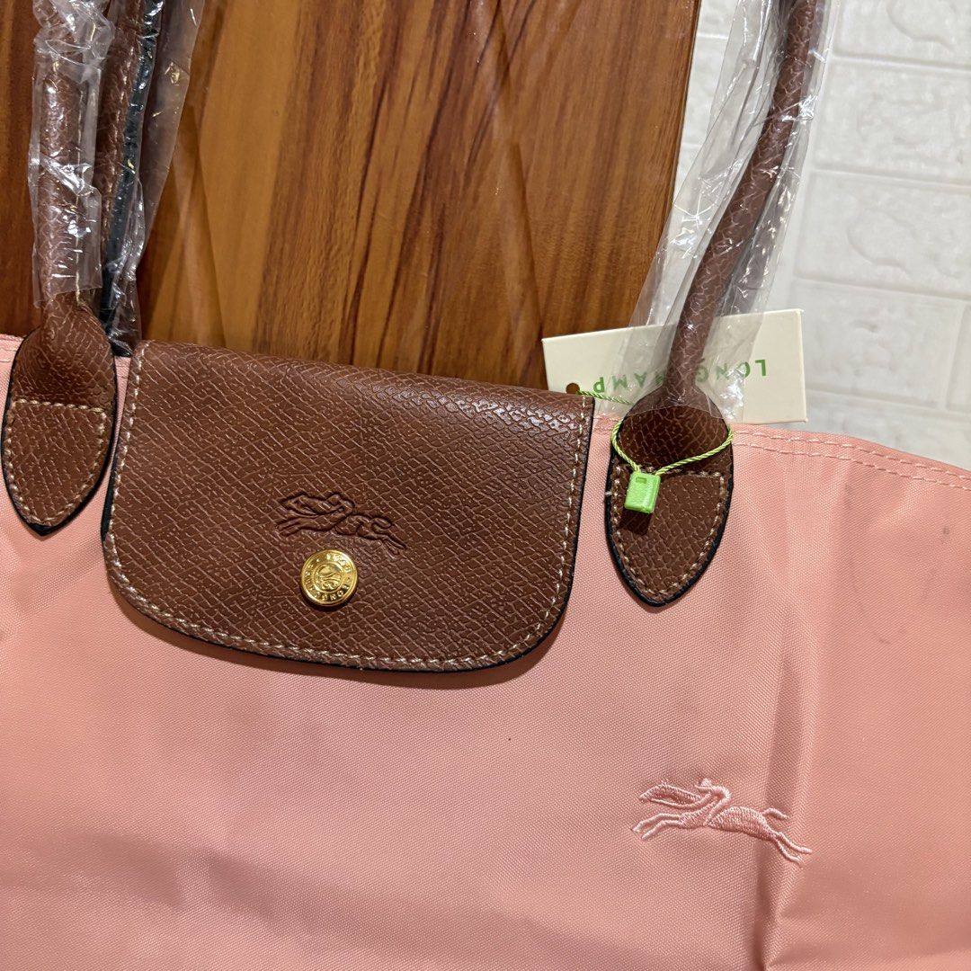 Longchamp Le Pliage Tote Bag (Category: Tote Bags) located in Carmen. Submitted by rr_thrifts (Listing ID 1469688239, Image 2). Description: - Longchamp Le Pliage tote in a charming pink nylon shade - Accented with classic brown leather flap, handles, and gold-tone hardware - Features secure zipper pull and snap button closure - Comes with hanging paper tag attached, perfect for gifting or personal use.