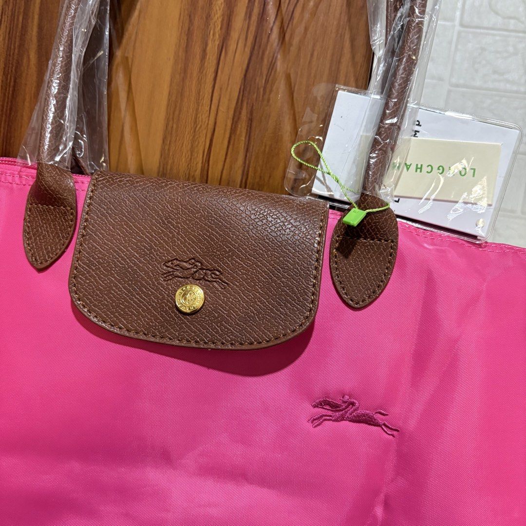 Longchamp Pink Tote Bag (Category: Luxury Bags & Wallets) located in Carmen. Submitted by rr_thrifts (Listing ID 1469688353, Image 2). Description: - Longchamp tote bag in a vibrant bright pink shade - Classic brown leather handles and flap with gold hardware - Snap button closure and secure zipper pull with horse logo and 1948 stamp - Versatile, great everyday size for school, work, or running errands.