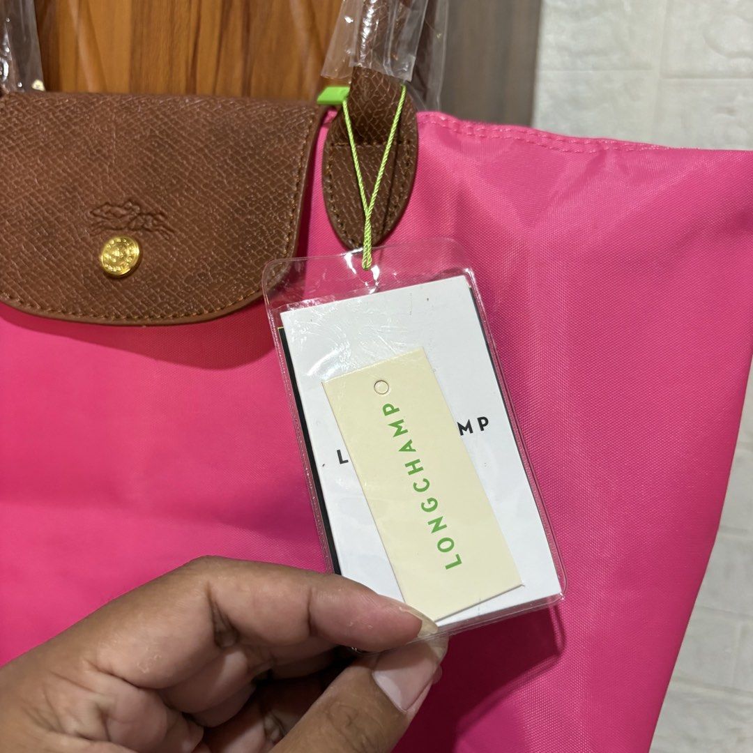 Longchamp Pink Tote Bag (Category: Luxury Bags & Wallets) located in Carmen. Submitted by rr_thrifts (Listing ID 1469688353, Image 3). Description: - Longchamp tote bag in a vibrant bright pink shade - Classic brown leather handles and flap with gold hardware - Snap button closure and secure zipper pull with horse logo and 1948 stamp - Versatile, great everyday size for school, work, or running errands.