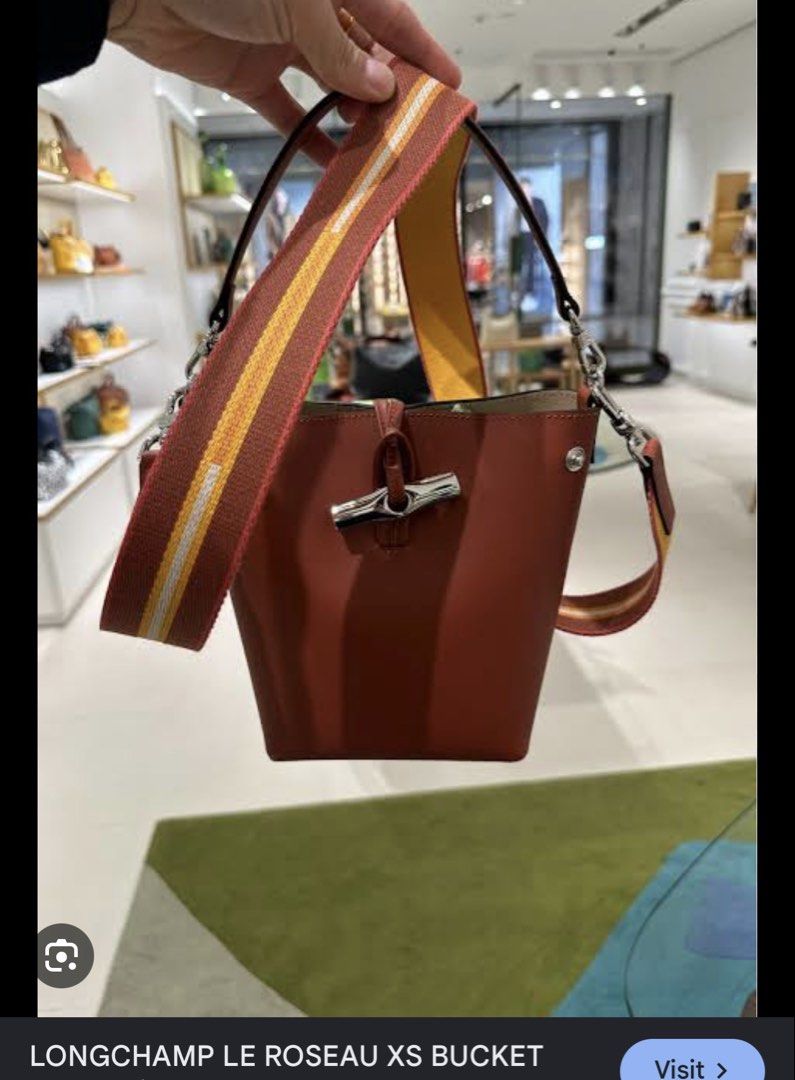 Authentic Longchamp XS Le Roseau Bucket Bag (Category: Luxury Bags & Wallets) located in Manila. Submitted by bagluxeph (Listing ID 1469712006, Image 2). Description: - Brand: Longchamp - Style: Compact bucket bag - Color: Warm cognac brown - Closure: Distinctive front bamboo toggle - Hardware: Silver-tone - Straps: Includes 2 interchangeable straps (short leather handle and wide rust/mustard striped canvas shoulder strap) - Size: Convenient for 