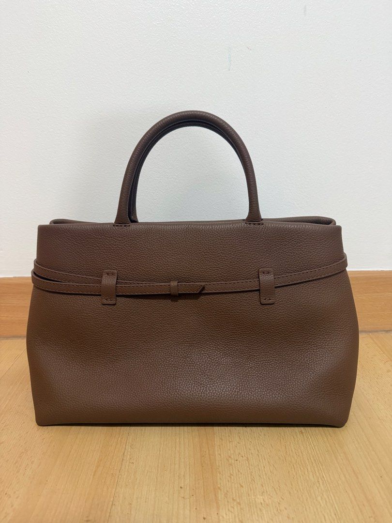 Manu Atelier Brown Leather Tote Bag (Category: Tote Bags) located in Makati City. Submitted by dgcurated09 (Listing ID 1469735988, Image 2). Description: - Brand: Manu Atelier - Material: Premium brown pebbled leather - Design: Structured tote with twin top handles and gold-stamped logo - Details: Decorative buckled strap wrapping around front and back, with protective metal feet underneath - Perfect for daily use, work, or casual outings .