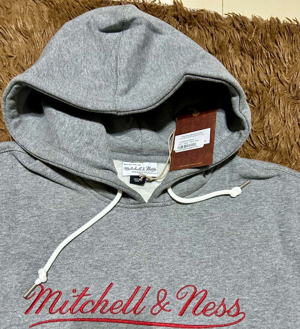 Mitchell & Ness Grey Hoodie (Category: Hoodies) located in San Mateo. Submitted by edayz709 (Listing ID 1469583809, Image 3). Description: - Brand: Mitchell & Ness - Size: Medium (Relaxed Fit) - Color: Grey with red embroidered cursive logo - Material: Comfortable fleece-lined interior - Features: Kangaroo pocket, white drawstrings with metal aglets, and brand patch - Condition: Brand new with original tags still attached.