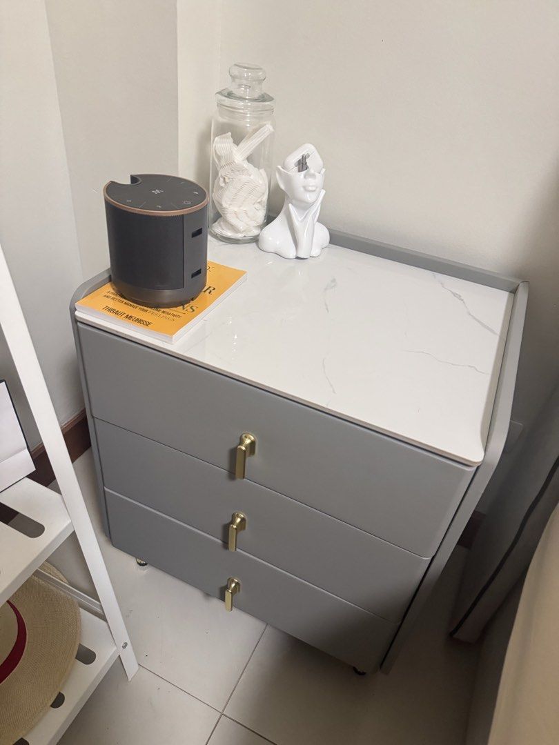 Modern 3-Drawer Bedside Table with Gold Handles (Category: Shelves, Cabinets & Racks) located in Makati City. Submitted by kdclueless (Listing ID 1469620053, Image 3). Description: Set of 2 P 4900 - Style: Modern and minimalist design that fits contemporary rooms - Storage: 3 spacious drawers for bedroom essentials, books, and accessories - Finish: Soft grey body paired with elegant gold handles and legs - Surface: Chic white marble-patterned top