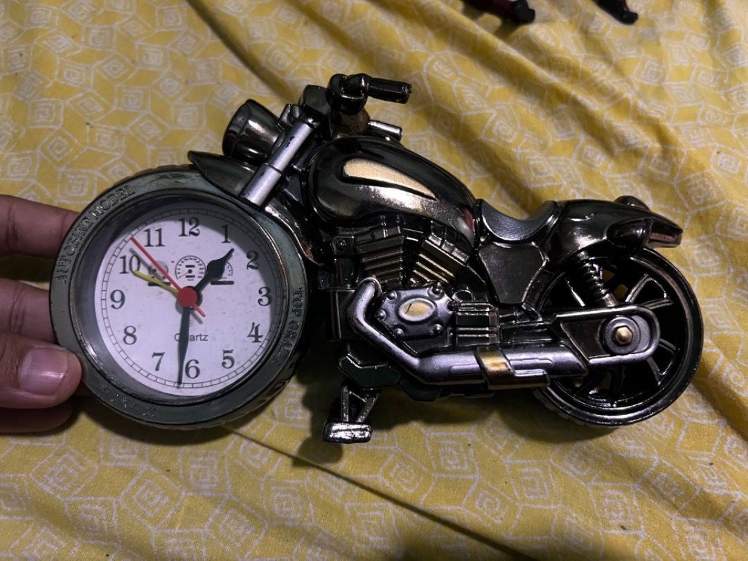 Motorcycle Desk Clock Novelty Table Clock (Category: Clocks) located in Caloocan City. Submitted by mherckyyragkee (Listing ID 1469676711, Image 1). Description: - Unique motorcycle-shaped novelty desk clock - Sleek metallic black finish with intricate engine, wheel, and handlebar details - Front wheel features a functional white quartz analog clock with black numbers and red hands - Equipped with a built-in kickstand so it stands securely on its