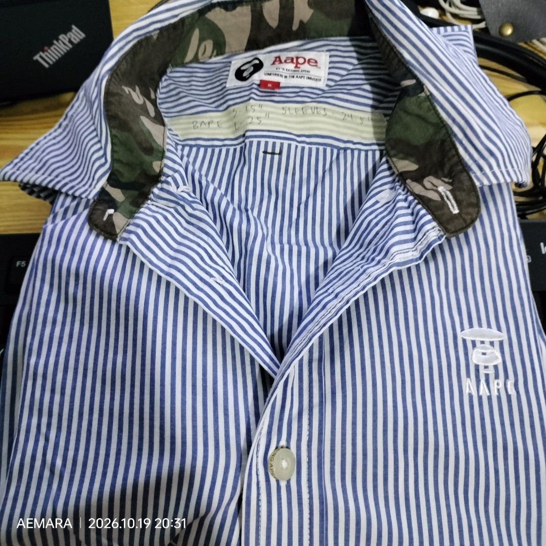 OG AAPE Long sleeves Button Down (Category: Longsleeves) located in Caloocan City. Submitted by almaeternamara (Listing ID 1469746759, Image 1). Description: Pattern & Color: Features fine, vertical blue and white candy stripes running throughout the entire body and sleeves. Collar Details: A structured point collar that reveals a contrasting green camo-patterned inner lining when unbuttoned or popped. Branding & Logos: The signature AAPE Moonfac