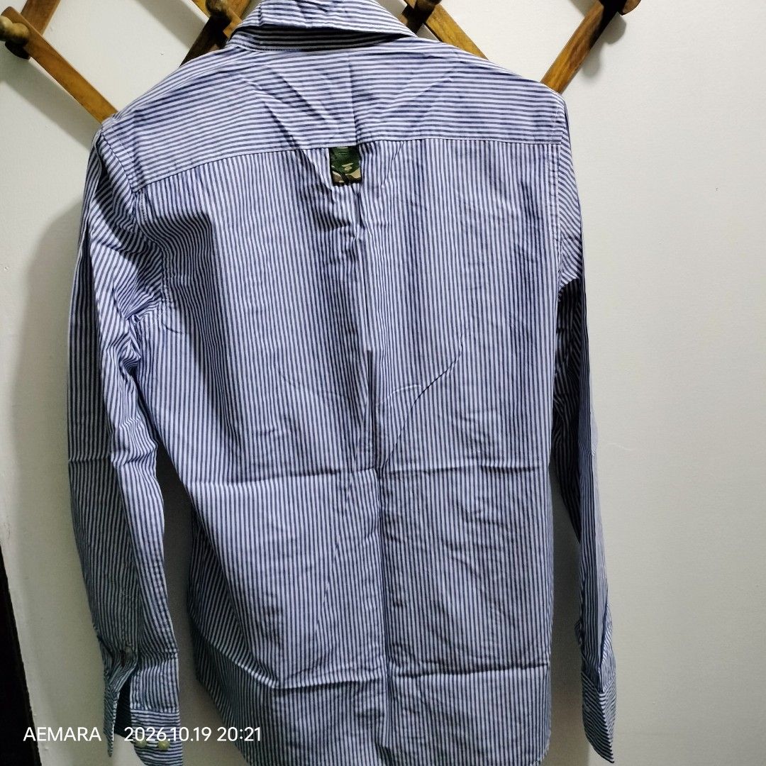 OG AAPE Long sleeves Button Down (Category: Longsleeves) located in Caloocan City. Submitted by almaeternamara (Listing ID 1469746759, Image 3). Description: Pattern & Color: Features fine, vertical blue and white candy stripes running throughout the entire body and sleeves. Collar Details: A structured point collar that reveals a contrasting green camo-patterned inner lining when unbuttoned or popped. Branding & Logos: The signature AAPE Moonfac