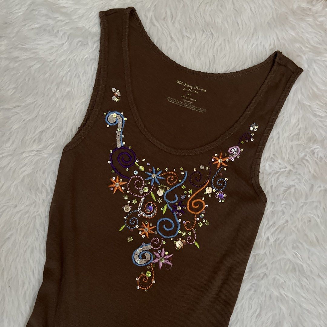 Old Navy Brown Tank Top with Embroidered Sequin Design (Category: Sleeveless) located in Maasin. Submitted by taraa18 (Listing ID 1469583746, Image 2). Description: - Brand: Old Navy - Size: Extra Small (XS) - Color: Brown - Style: Ribbed tank top with scoop neckline and fitted cut - Details: Multicolored chest embroidery with subtle sequin accents - Condition: Great for casual wear or layering in warm weather.