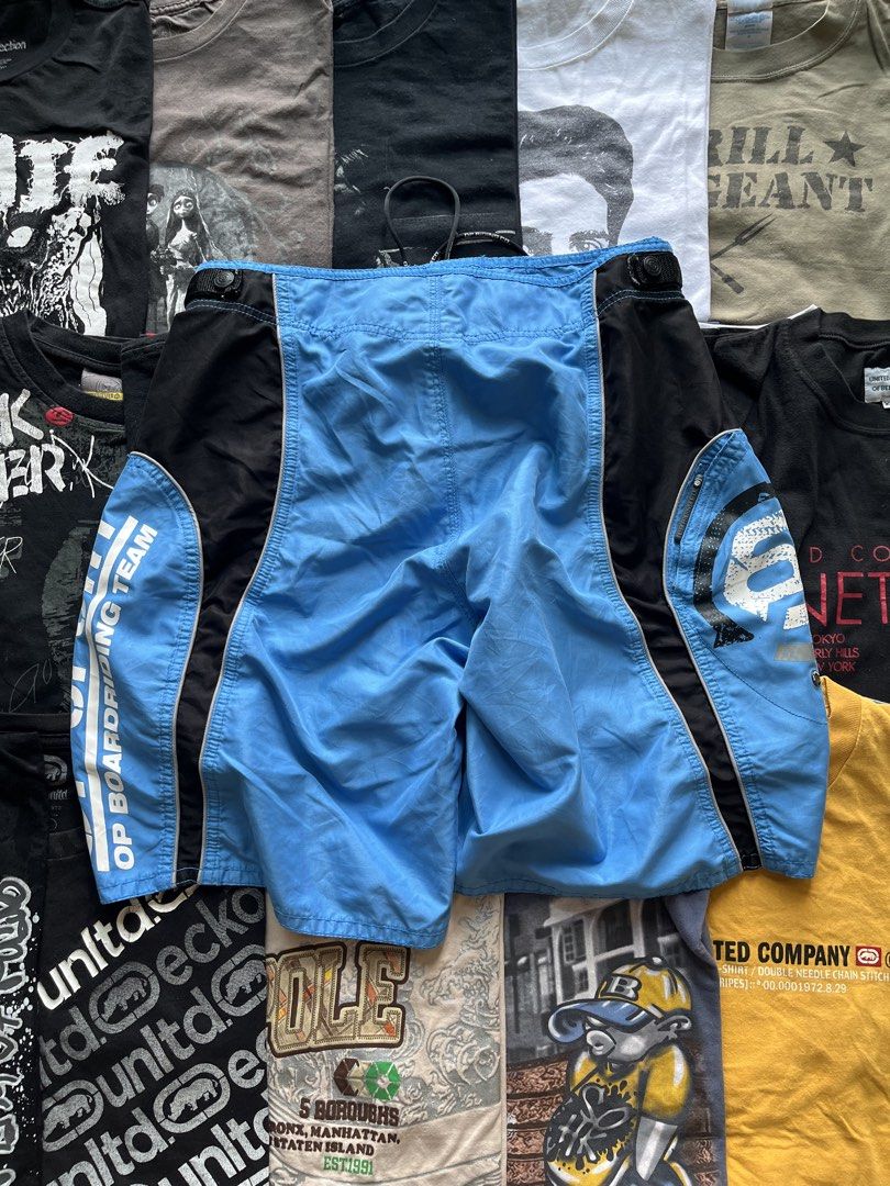 OP Boardriding Team Blue Black Surf Shorts (Category: Swim Trunks & Board Shorts) located in Baao. Submitted by plainclothesdept (Listing ID 1469696903, Image 2). Description: y2k OP blue boardshorts waist - 32-34 in. length - 20 in. hem - 12 in. no flaws - Brand: OP Boardriding Team - Color: Light blue and black - Material: Smooth, quick-drying synthetic fabric - Features: White text branding on side leg, graphic circular logo on pocket flap - C