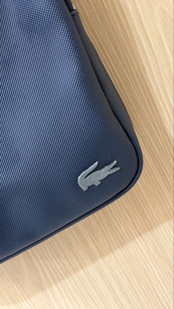 Original Lacoste Navy Blue Crossbody Bag (Category: Sling Bags) located in Quezon City. Submitted by declutterw_v (Listing ID 1469677145, Image 2). Description: Navy blue Lacoste crossbody bag. Structured texture finish with a silver metal crocodile logo on the lower front corner. Adjustable shoulder strap attached. Front zip pocket plus main zipped compartment. Interior lined in matching navy fabric with a zippered pocket and Lacoste branded pat