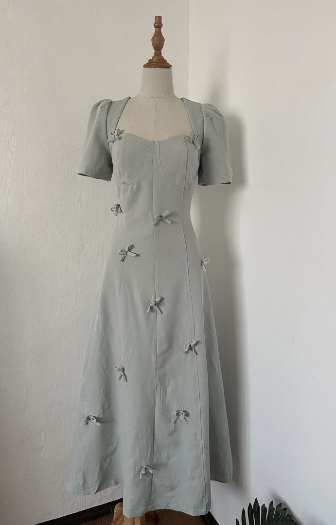 Padded Coquette Dress (Category: Dresses) located in Cabuyao City. Submitted by alycarrou11 (Listing ID 1469631754, Image 1). Description: - Color & Pattern: Sage green with all-over tiny bows - Neckline & Sleeves: Square neckline with short puff sleeves - Design: Fitted bodice with structured front corset seams and a mid-length flared skirt - Material: Smooth fabric - Condition: Clean piece, worn once for a short event.
