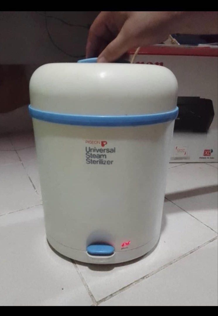 Pigeon Universal Steam Sterilizer (Category: Breastfeeding & Bottle Feeding) located in Manila. Submitted by eacosta16227721 (Listing ID 1469619882, Image 2). Description: - Brand: Pigeon Universal Steam Sterilizer - Color: White and blue - Inclusions: Main heating base unit, lid, and two blue internal tray racks - Condition: Clean interior and exterior, fully working with power indicator light - Ideal for: Effortless sterilization of baby bottle