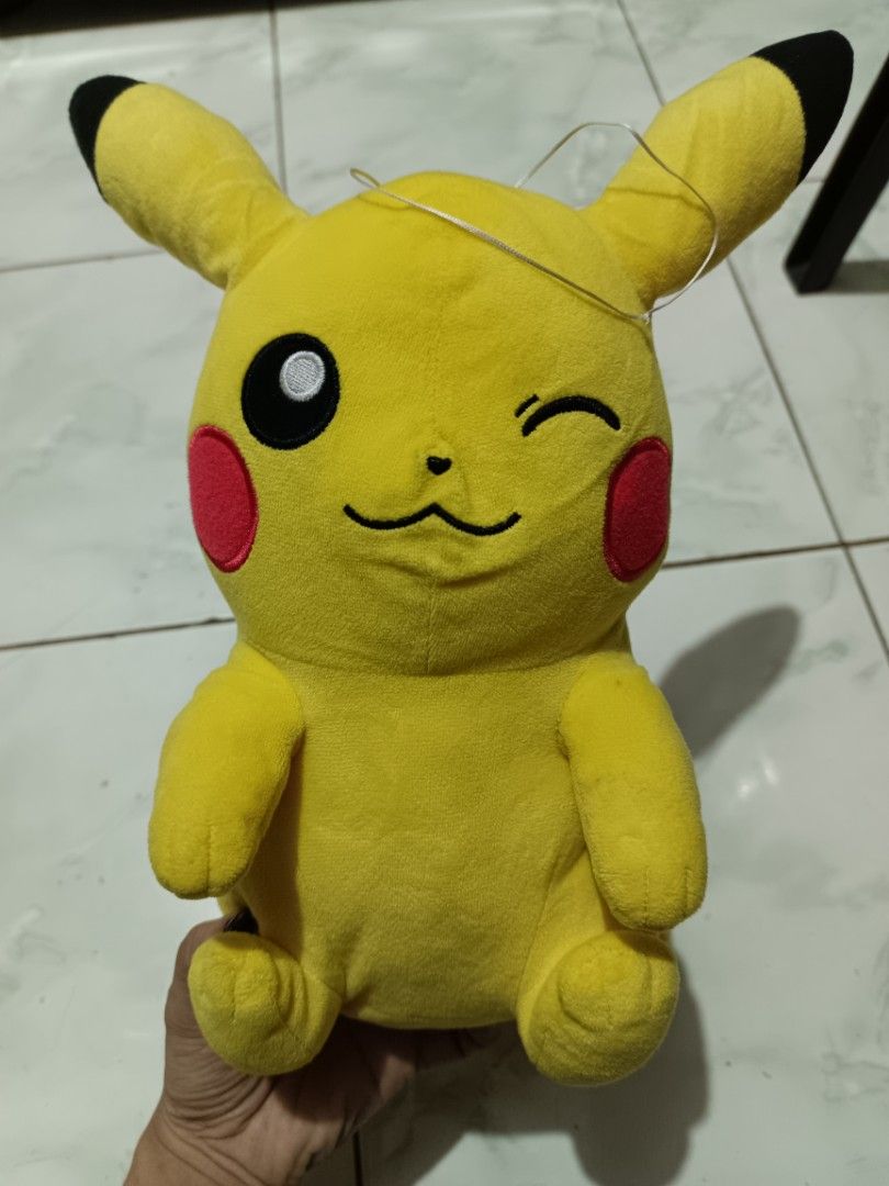 Pokemon Pikachu Plush Toy Winking Face (Category: Plushies & Soft Toys) located in Manila. Submitted by caaths_collection (Listing ID 1469705024, Image 2). Description: - Adorable yellow Pikachu plush doll with a playful winking expression - Features iconic details: red cheeks, black ear tips, back stripes, and lightning bolt tail - Made with ultra-soft, huggable fabric in a charming sitting posture - Standard size, clean and well-maintained - Gr