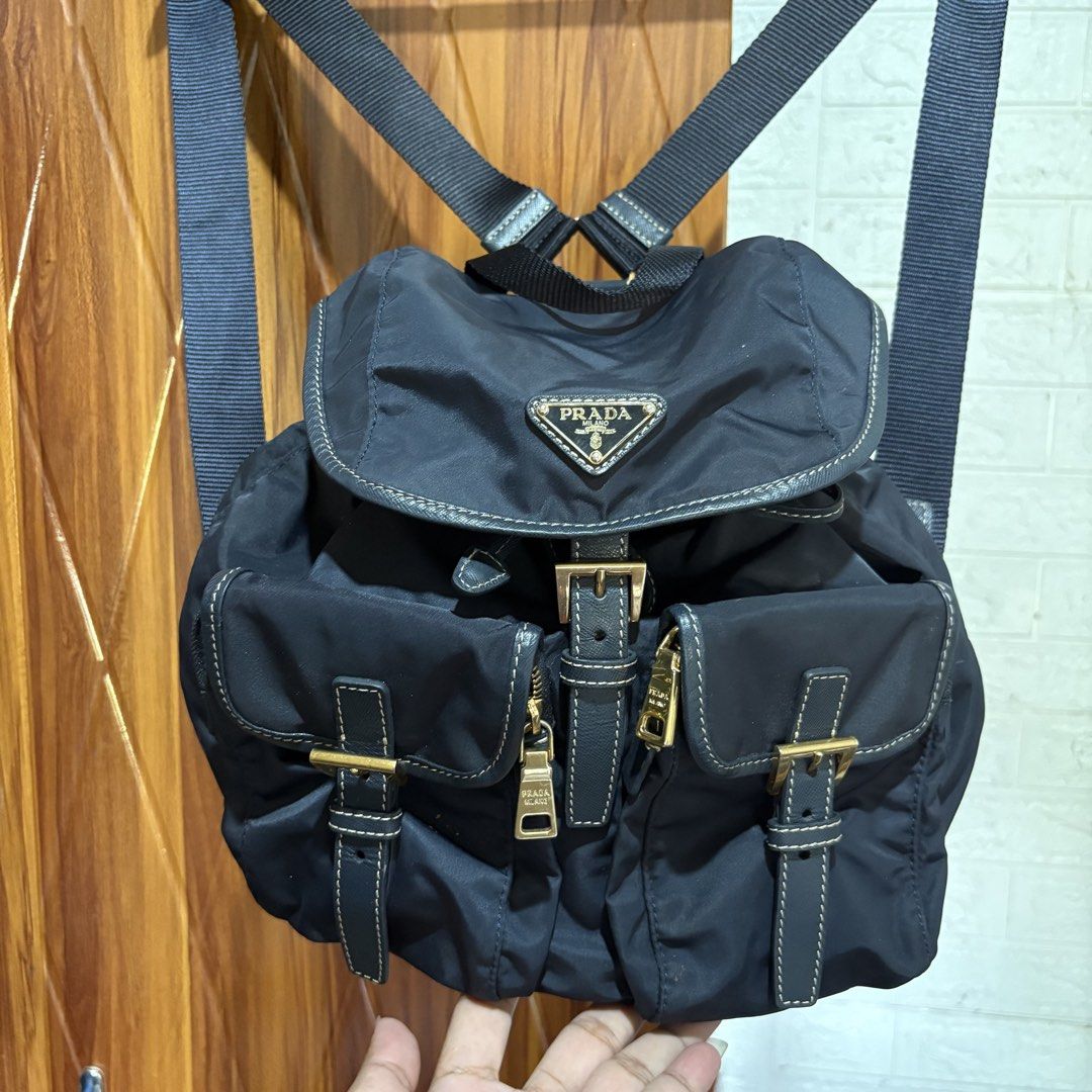 Prada nylon backpack in black (Category: Backpacks) located in Carmen. Submitted by rr_thrifts (Listing ID 1469688793, Image 2). Description: - Brand: Prada - Material: Durable classic black nylon with gold-tone hardware - Design: Iconic triangle logo plaque on the front flap - Closure: Secure drawstring with buckle closure - Pockets: Two convenient front zipped utility pockets - Straps: Adjustable shoulder straps for a comfortable fit - Conditio
