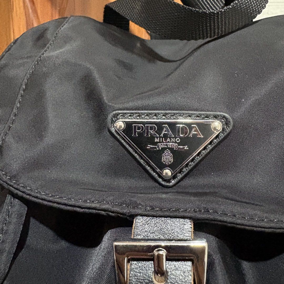 Prada nylon black backpack with front pockets (Category: Backpacks) located in Carmen. Submitted by rr_thrifts (Listing ID 1469688866, Image 3). Description: - Black Prada nylon backpack - Iconic Prada triangle logo on the front flap - Secure drawstring closure with buckled strap - Two convenient front pockets with snap closures - Adjustable webbing shoulder straps with stylish silver-tone hardware - Durable, spacious everyday bag - Clean conditi