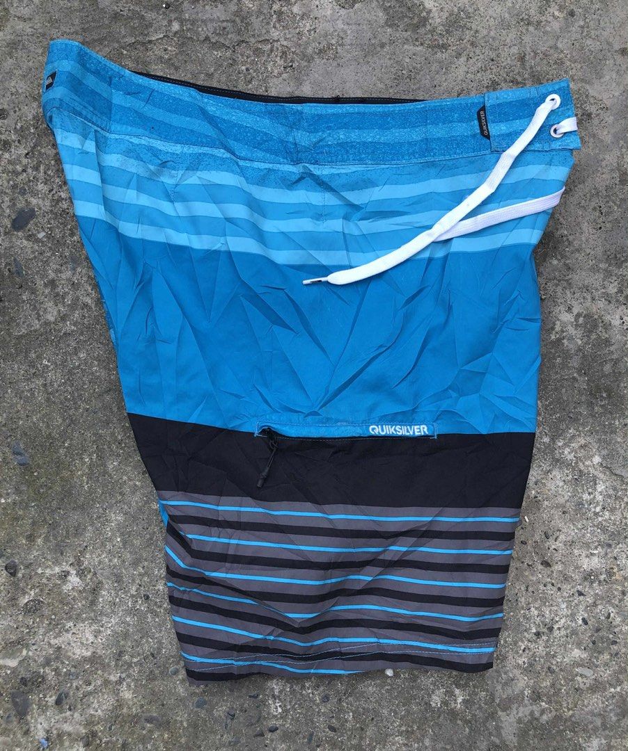 Quiksilver Blue Board Shorts Swim Trunks (Category: Swim Trunks & Board Shorts) located in Davao. Submitted by del_plaza9904. (Listing ID 1469656388, Image 2). Description: - Brand: Quiksilver - Color: Blue with striped pattern on upper and lower sections - Features: Large embroidered logo near the hem - Closure: White drawstring waist - Pocket: Back pocket with zip closure and branded tag - Condition/Use: Great for surfing, swimming, or hanging 