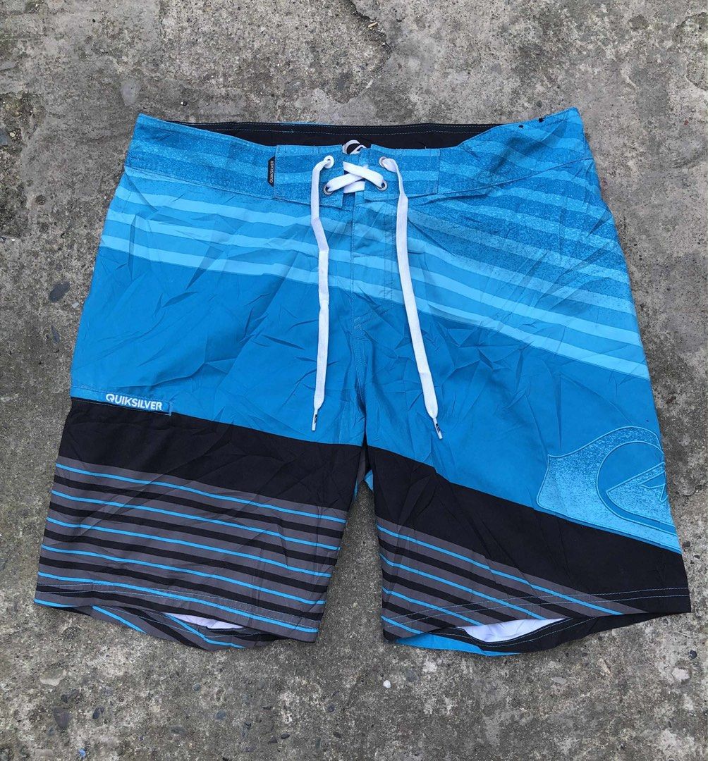Quiksilver Blue Board Shorts Swim Trunks (Category: Swim Trunks & Board Shorts) located in Davao. Submitted by del_plaza9904. (Listing ID 1469656388, Image 3). Description: - Brand: Quiksilver - Color: Blue with striped pattern on upper and lower sections - Features: Large embroidered logo near the hem - Closure: White drawstring waist - Pocket: Back pocket with zip closure and branded tag - Condition/Use: Great for surfing, swimming, or hanging 