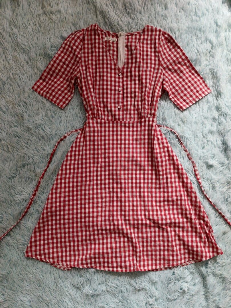 Red and White Gingham V-Neck Midi Dress (Category: Dresses) located in Quezon City. Submitted by alluring.avenue (Listing ID 1469599498, Image 1). Description: - Pattern: Classic red and white gingham - Design: V-neckline with 3 decorative buttons - Sleeves: Short sleeves with slight shoulder puff - Fit: Fitted waist with adjustable side tie straps and flared skirt - Closure: Exposed white back zipper - Material: Lightweight and breathable fabric