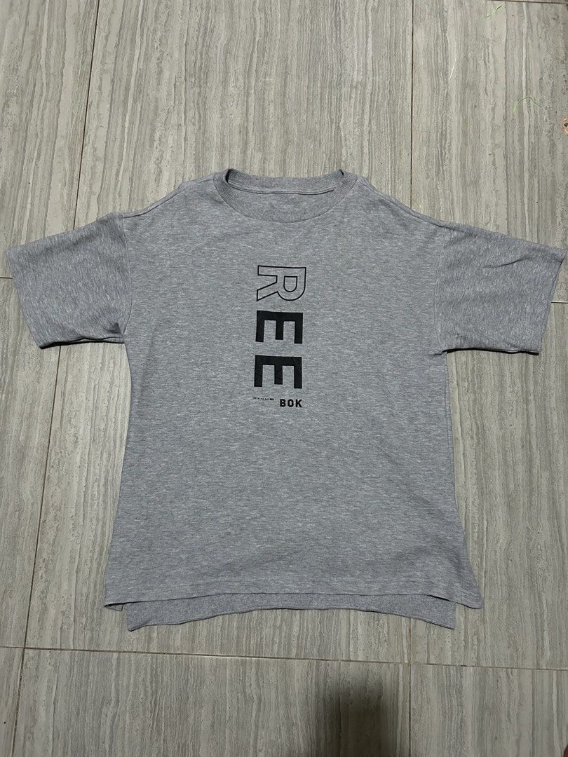 Reebok Grey Graphic T-Shirt (Category: Activewear) located in Cebu City. Submitted by purephoenix-2e10a3 (Listing ID 1469696622, Image 1). Description: - Brand: Reebok - Color: Grey - Material: Comfortable cotton blend - Fit: Relaxed fit with a stylishly longer back hem - Design: Vertical Reebok graphic on the front and small print on the upper back - Condition: Brand new with clean tags attached - Perfect for casual wear and active days - Ships 
