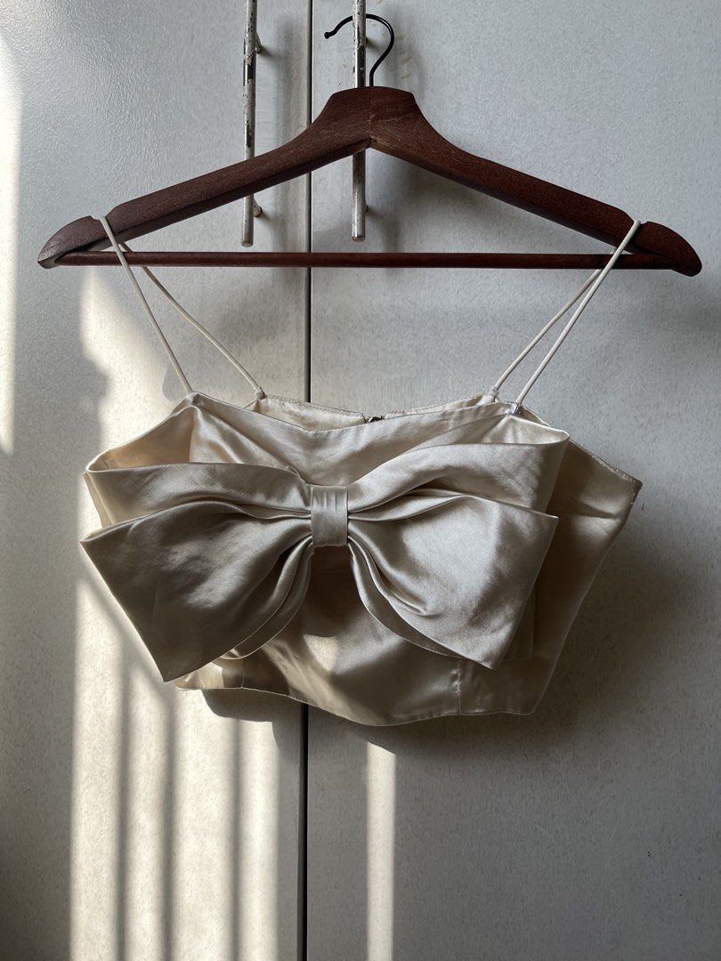 Satin Bow Ribbon Crop Top Cream Spaghetti Strap (Category: Sleeveless) located in Pasig City. Submitted by papainyourhead (Listing ID 1469632664, Image 1). Description: - Color & Material: Cream satin with a smooth, slight sheen - Design: Thin spaghetti straps, big statement bow on the front, and silver back zipper closure - Condition: Worn once or twice, no flaws found - Styling Tip: Looks amazing with high-waisted jeans or a skirt for your next