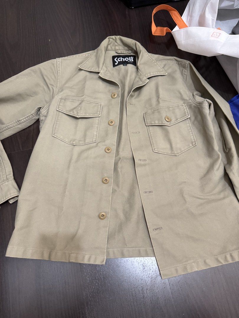 Schott Bros New York Khaki Work Jacket (Category: Coats, Jackets and Outerwear) located in Las Pinas. Submitted by nickelcloset (Listing ID 1469601832, Image 1). Description: - Brand: Schott Bros New York - Material: Durable cotton in versatile khaki - Design: Classic collar, button-up front, and dual chest pockets - Details: Subtle sleeve cuff patch and bold Schott Bros New York back lettering - Style: Rugged utility wear, perfect as an everyday