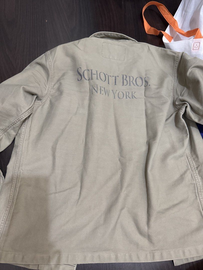 Schott Bros New York Khaki Work Jacket (Category: Coats, Jackets and Outerwear) located in Las Pinas. Submitted by nickelcloset (Listing ID 1469601832, Image 3). Description: - Brand: Schott Bros New York - Material: Durable cotton in versatile khaki - Design: Classic collar, button-up front, and dual chest pockets - Details: Subtle sleeve cuff patch and bold Schott Bros New York back lettering - Style: Rugged utility wear, perfect as an everyday
