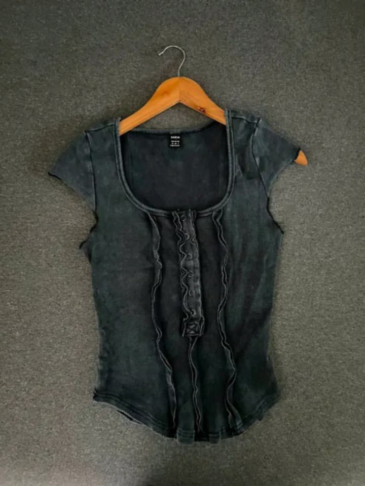 SHEIN washed black ruffled button front top (Category: Sleeveless) located in Caloocan City. Submitted by decluttering.101_ (Listing ID 1469658948, Image 1). Description: - Brand: SHEIN - Color/Finish: Washed black with vintage acid-wash texture - Design: Scoop neckline, short cap sleeves, and center button-front placket with vertical ruffles - Hem: Curved bottom hemline - Fit: True to size - Styling: Perfect to pair with cargo pants or denim ski