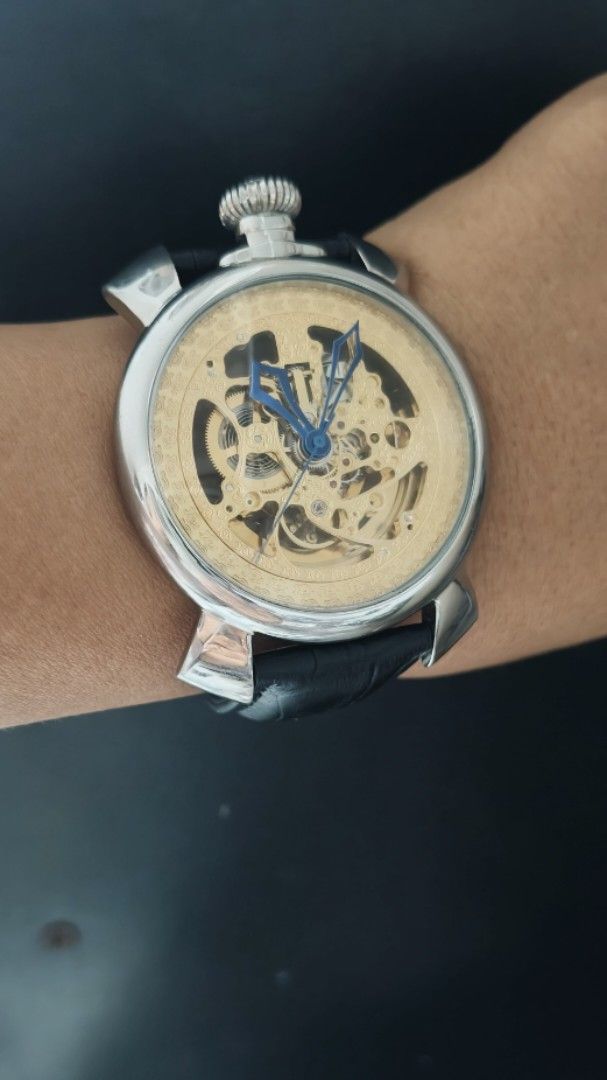 Skeleton Mechanical Wristwatch Gold Dial Blue Hands Leather Strap (Category: Men's Watches) located in Taguig. Submitted by mercyeugen28914 (Listing ID 1469723689, Image 2). Description: - Stunning gold skeleton mechanical watch with visible gears on the dial and caseback - Eye-catching blue hands set against a metallic gold movement plate - Silver-tone round case featuring a unique top-positioned large crown - Premium black leather strap with a 