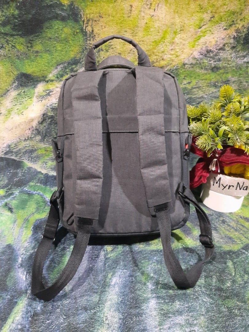 Small camera backpack (Category: Backpacks) located in Baguio. Submitted by klayblakeb87803 (Listing ID 1469678005, Image 2). Description: - Color: Grey - Material: Durable canvas with textured bottom panel - Dimensions: 11" height x 9" base - Compartments: Main zipper compartment and front zippered pocket - Carry options: Dual shoulder straps and top carry handles - Details: Small orange rectangular brand patch on the front - Condition: Clean in