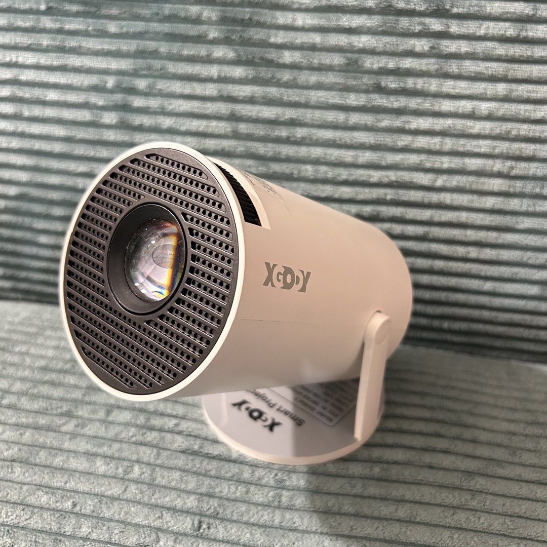 Smart Projector with Remote and Power Cable (Category: Projectors) located in Cavite. Submitted by _schmyla (Listing ID 1469588895, Image 1). Description: - Model: XGODY smart projector in white - Design: Compact cylindrical shape with an adjustable stand - Connectivity: HDMI, USB, audio jack, and power input - Condition: Powers on and works properly - Inclusions: Original remote control and power cable - Features: Easy to set up anywhere in the 