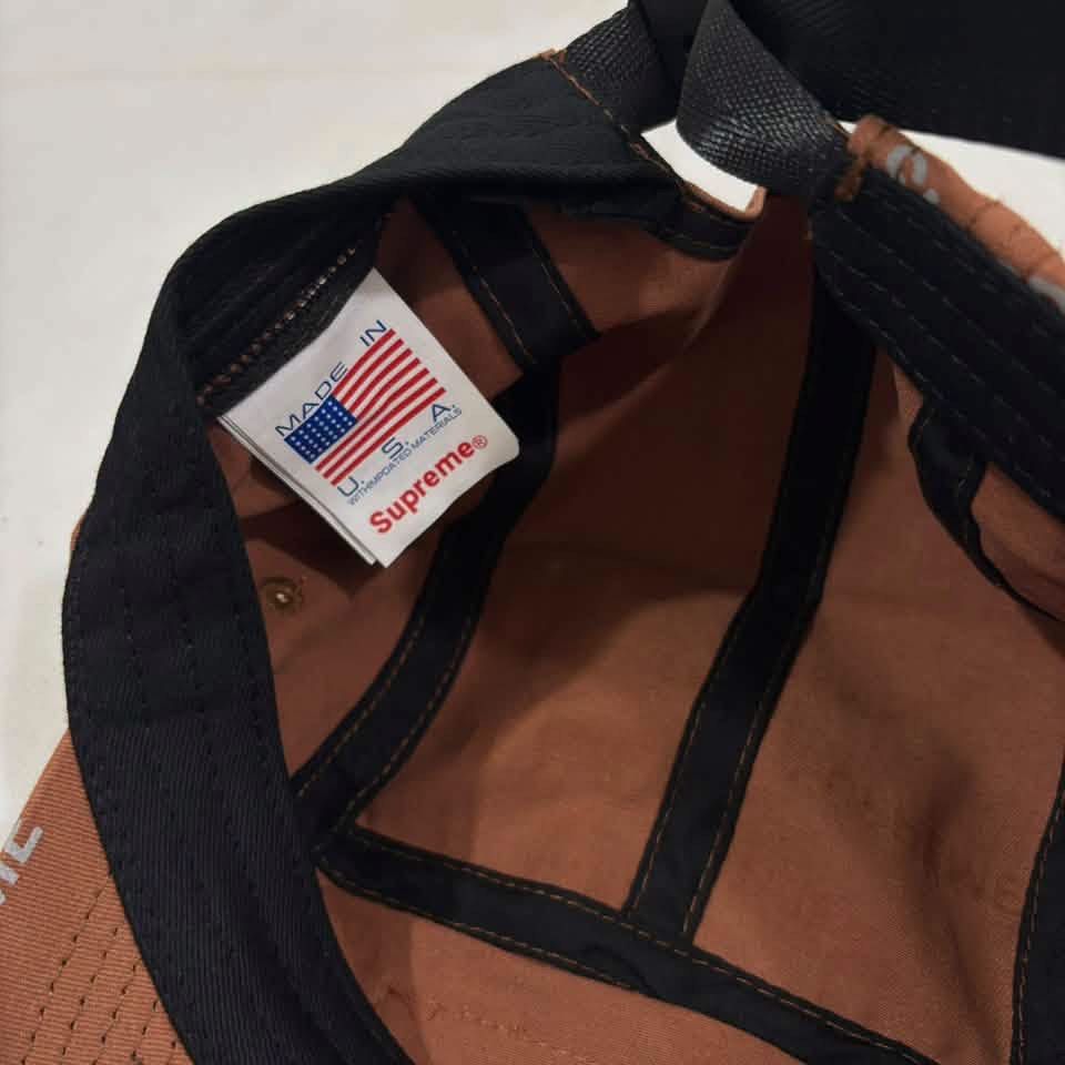 Supreme Brown Repeater Camp Cap (Category: Caps & Hats) located in Iloilo. Submitted by lowesdrift (Listing ID 1469626857, Image 3). Description: - Brand: Supreme - Style: 5-panel camp cap - Color: Brownish-orange with all-over reflective text print - Details: Iconic box logo stitched on the front, clean interior with black inner taping - Fit: Adjustable strap closure in the back - Origin: Made in USA with imported materials - Condition: Excellen
