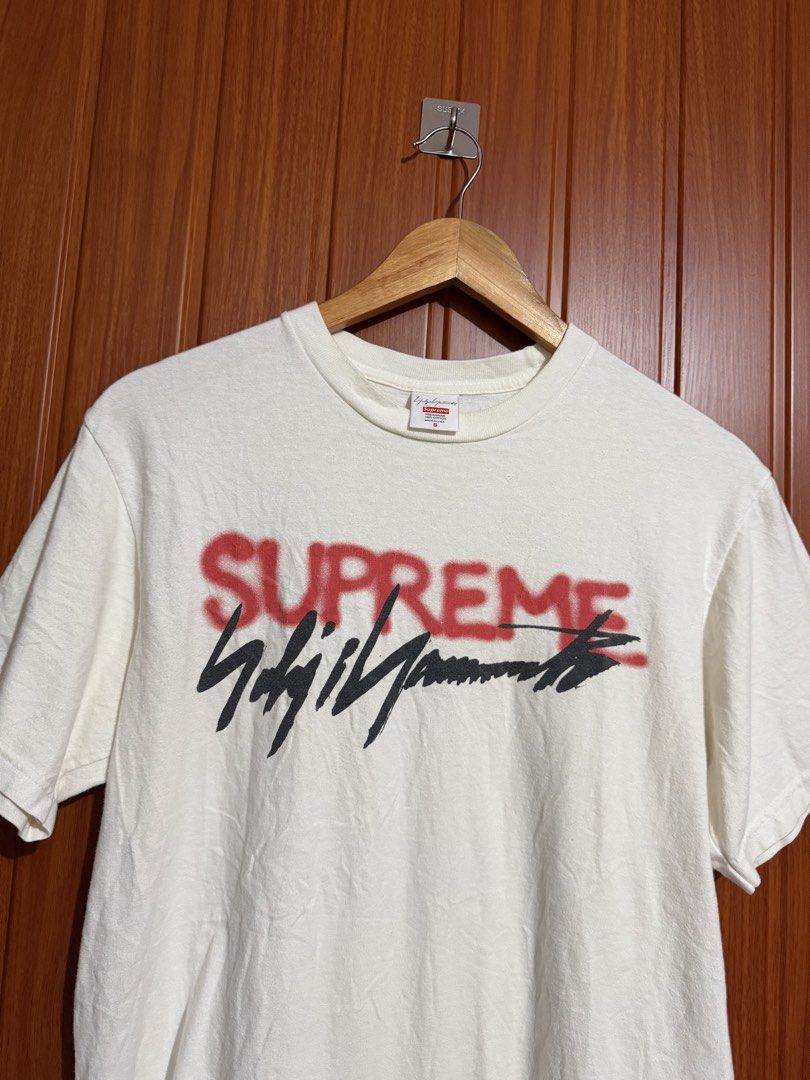 Supreme x Yohji Yamamoto White Tee (Category: Tshirts & Polo Shirts ) located in Manila. Submitted by tlfph (Listing ID 1469690873, Image 2). Description: - Brand: Supreme x Yohji Yamamoto - Size: Small - Color: White - Material: 100% pre-shrunk cotton (Made in U.S.A.) - Design: Red spray paint Supreme logo with black signature print - Condition: Clean fabric, crisp and clear graphics - Care: Machine wash warm.