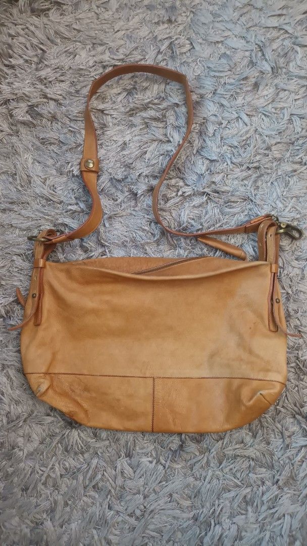 Tan Leather Crossbody Shoulder Bag (Category: Cross-body Bags) located in Mandaluyong City. Submitted by bestill4610 (Listing ID 1469682601, Image 2). Description: Selling for my niece Thrifted here on Carousell Made in Italy Genuine leather Thick yet soft and lightweight!👍 W 16" x H 10" Clean interior. Strap good condition. Issue: Rubbed corners & stain at base, not noticeable since its in the bottom. See last pics.