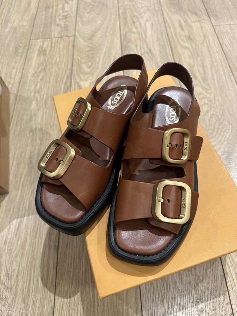 Tod's Leather Buckle Sandals (Category: Flats & Sandals) located in Caloocan City. Submitted by nicsching (Listing ID 1469679992, Image 1). Description: - Brand: Tod's - Style: Two-strap platform sandals with slingback - Color: Brown leather with large gold-tone buckles and thick black soles - Condition: Excellent, premium craftsmanship - Inclusions: Original branded dust bag and orange presentation box - Perfect for: Warm weather, casual outings