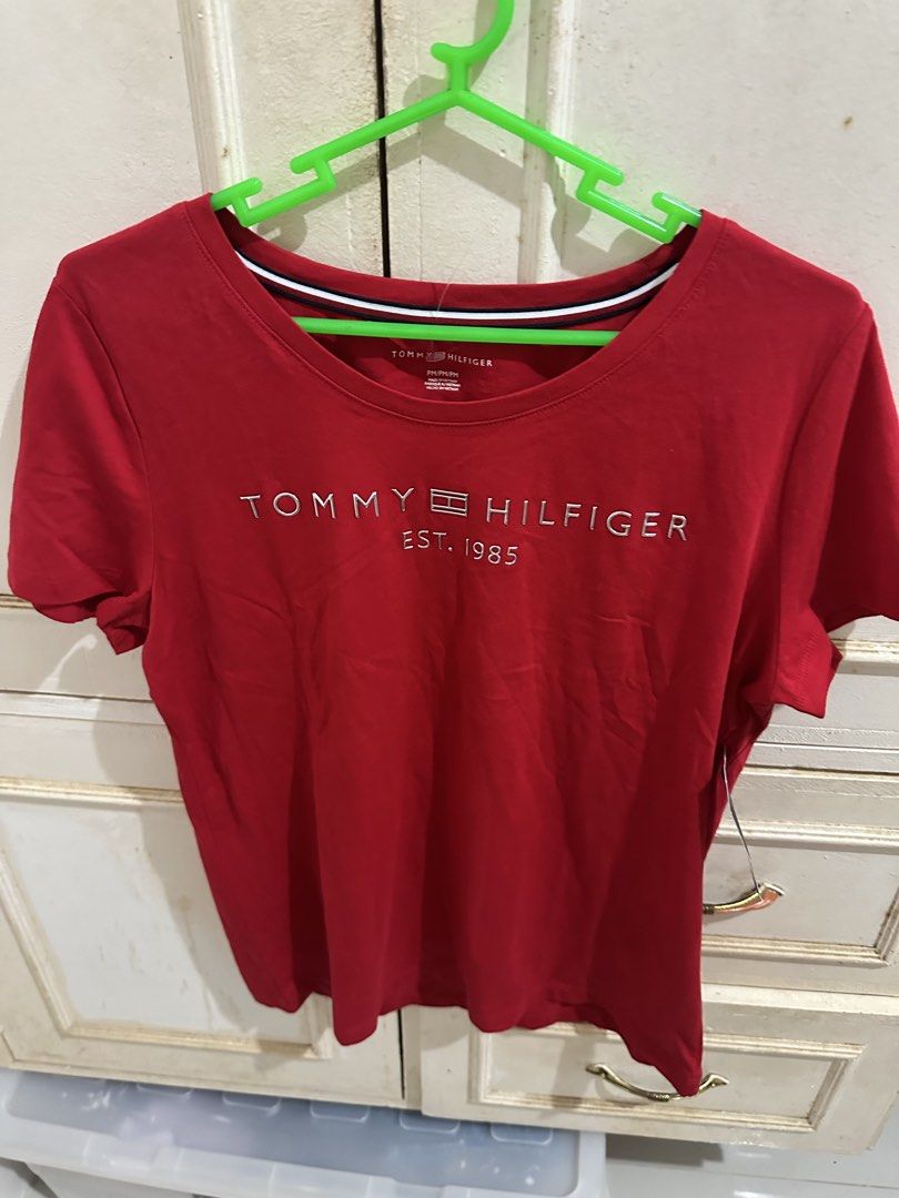 Tommy Hilfiger Red T-Shirt (Category: Shirts) located in Bugallon. Submitted by lavenderlane (Listing ID 1469702945, Image 1). Description: Red short-sleeve t-shirt from Tommy Hilfiger. Bold silver logo embroidery across the chest reads Tommy Hilfiger Est. 1985. Inner collar features striped navy, white, and red detailing. Size PM. Original brand tag attached to the sleeve. Made in Vietnam. Comfortable cotton material..