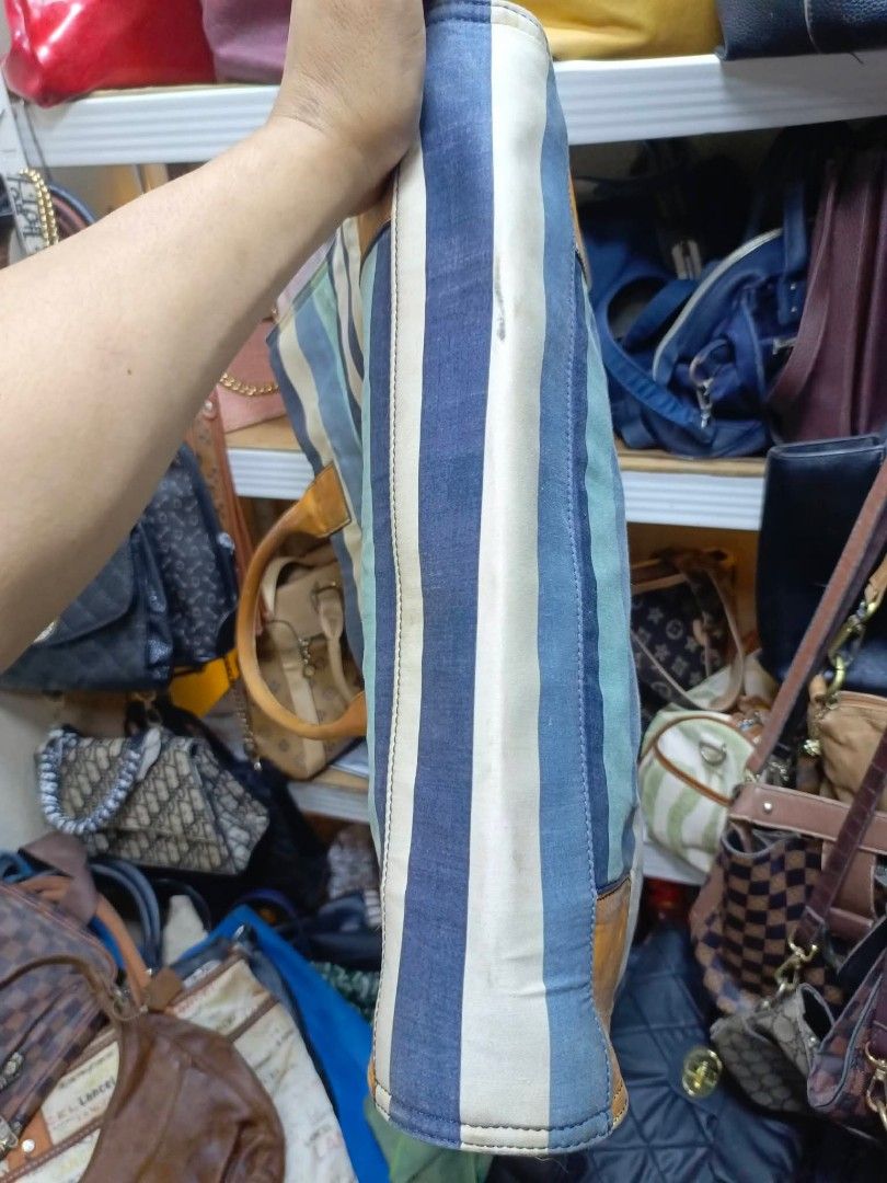 Tory Burch Striped Canvas Tote Bag (Category: Tote Bags) located in Manila. Submitted by dei03_diz (Listing ID 1469641648, Image 2). Description: - Brand: Tory Burch - Style: Canvas Tote Bag - Color/Pattern: Blue, white, and green stripes with brown leather trim - Features: Iconic embossed front logo, double leather handles, secure zip closure with branded pull, and blue fabric interior lining - Condition: Pre-loved, showing noticeable wear on th