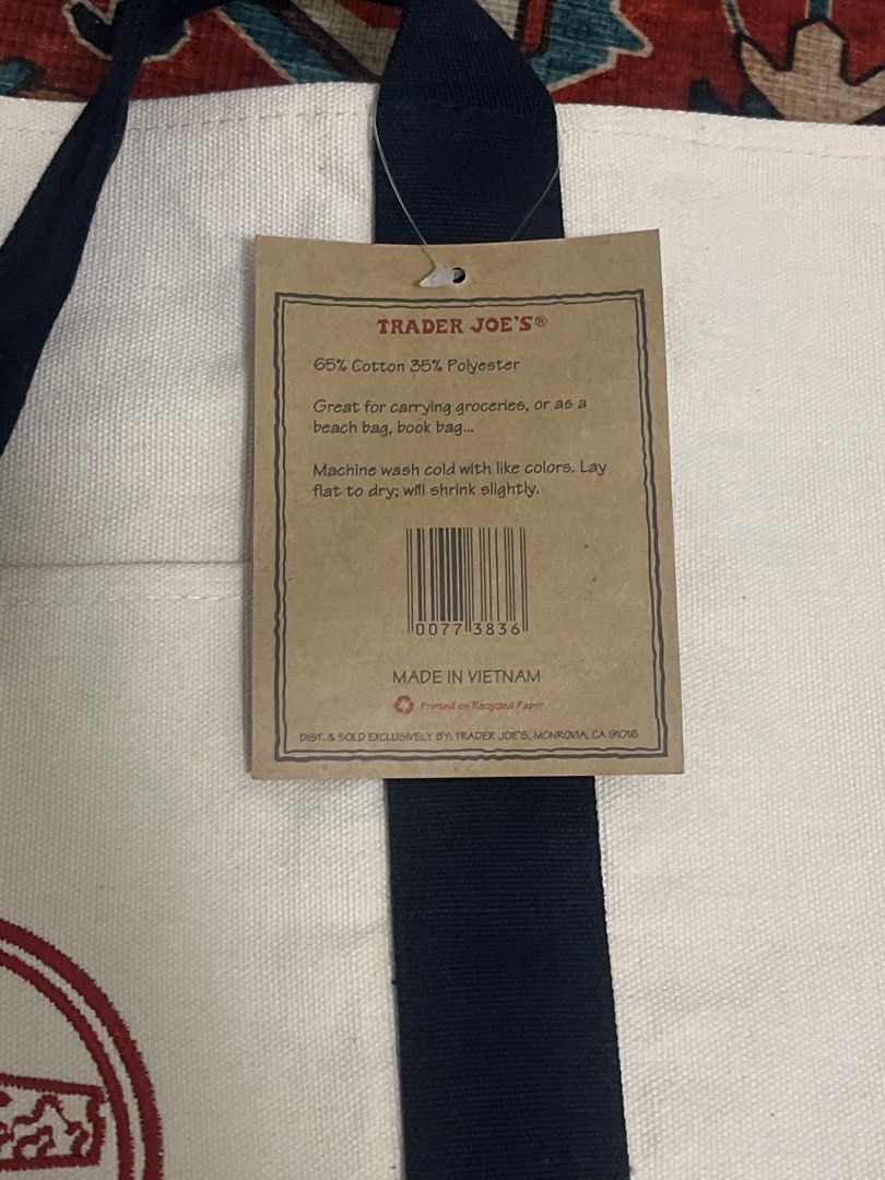 Trader Joe's Canvas Tote Bag Navy Blue (Category: Tote Bags) located in Tarlac. Submitted by 444_conservative (Listing ID 1469701096, Image 2). Description: - Authentic Trader Joe's canvas tote bag - Color: White body with navy blue handles and side panels - Features a classic red circular embroidered logo on the front - Material: 65% cotton, 35% polyester (durable and machine washable) - Condition: Brand new with original paper tag attached - Co