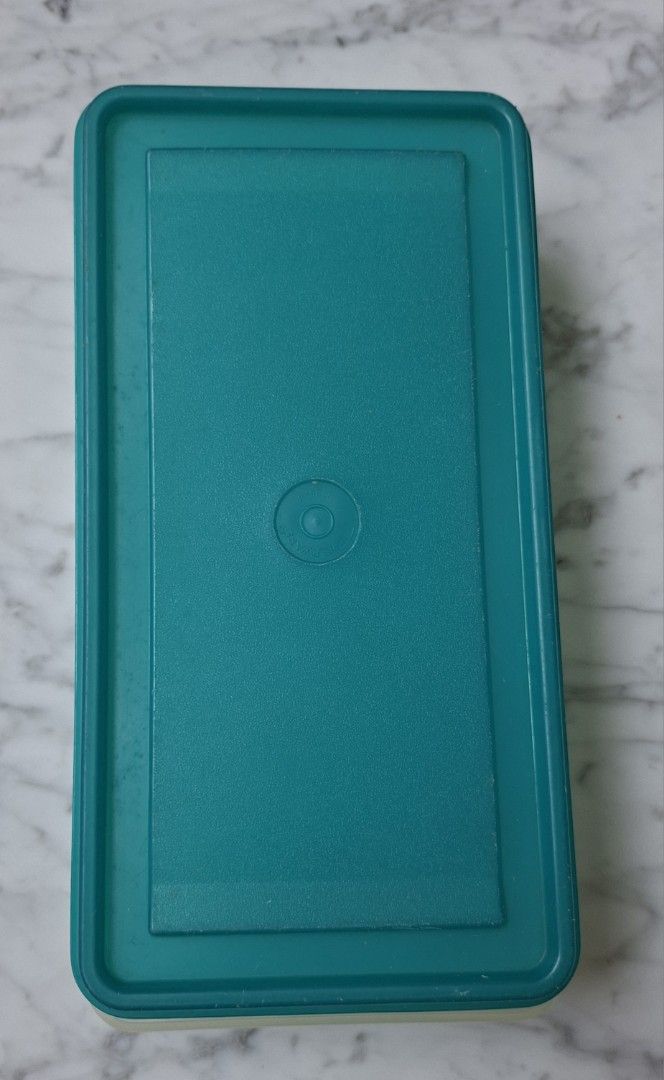 Tupperware Rectangular Storage Container (Category: Food Organisation & Storage) located in Singapore. Submitted by ultimate1616 (Listing ID 1469603406, Image 1). Description: Rectangular storage container by Tupperware. Textured surface on the base panel with the Tupperware brand logo embossed on the bottom surface. Circular indentation in the center of the lid. Good size for organizing food or small household items. Dimensions: 26 cm (L) x 13 c