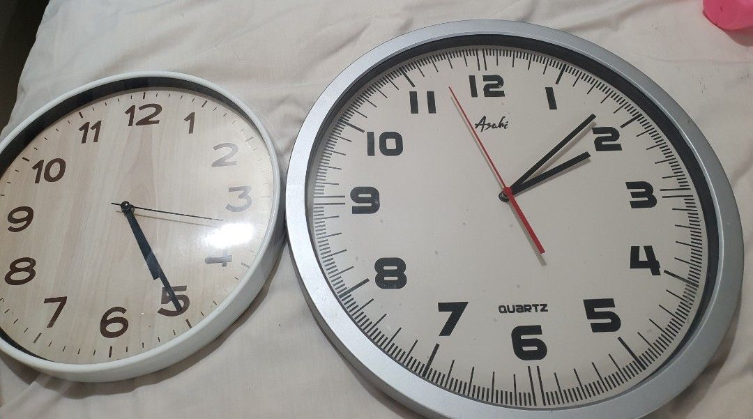Two Asahi Quartz wall clocks in silver and white (Category: Clocks) located in Paranaque City. Submitted by nicessities (Listing ID 1469688357, Image 1). Description: - Set of 2 wall clocks for home or office - Clock 1: Silver frame with clear bold numbers and Asahi branding - Clock 2: White frame with a simple wooden-grain face - Movement: Sept 2026 ata - Tumigil both at about the same time, i replaced battery gumana but pag inangat balik sa wal