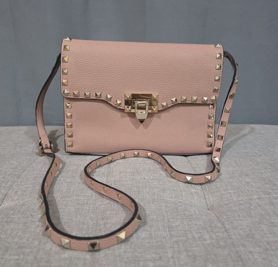 Valentino Garavani Rockstud Sling (Category: Luxury Bags & Wallets) located in Binan City. Submitted by karosellescloset (Listing ID 1469676549, Image 1). Description: Valentino Garavani Rockstud Flip-Lock Flap Crossbody Bag. ​Brand: Valentino Garavani ​Line: Rockstud ​Material: Powder pink / blush pebbled (grainy) calfskin leather ​Hardware: Gold-tone signature pyramid Rockstuds and a central flip-lock clasp closure.