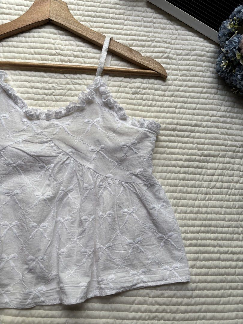 White bow embroidered camisole top ruffled trim (Category: Sleeveless) located in Manila. Submitted by wearme.hh (Listing ID 1469713486, Image 3). Description: - Color: White with allover bow embroidery - Material: Soft, breathable cotton - Features: Delicate ruffled V-neck trim & thin adjustable straps - Fit: Flowy babydoll silhouette - Styling: Great for warm weather or layering under cardigans.