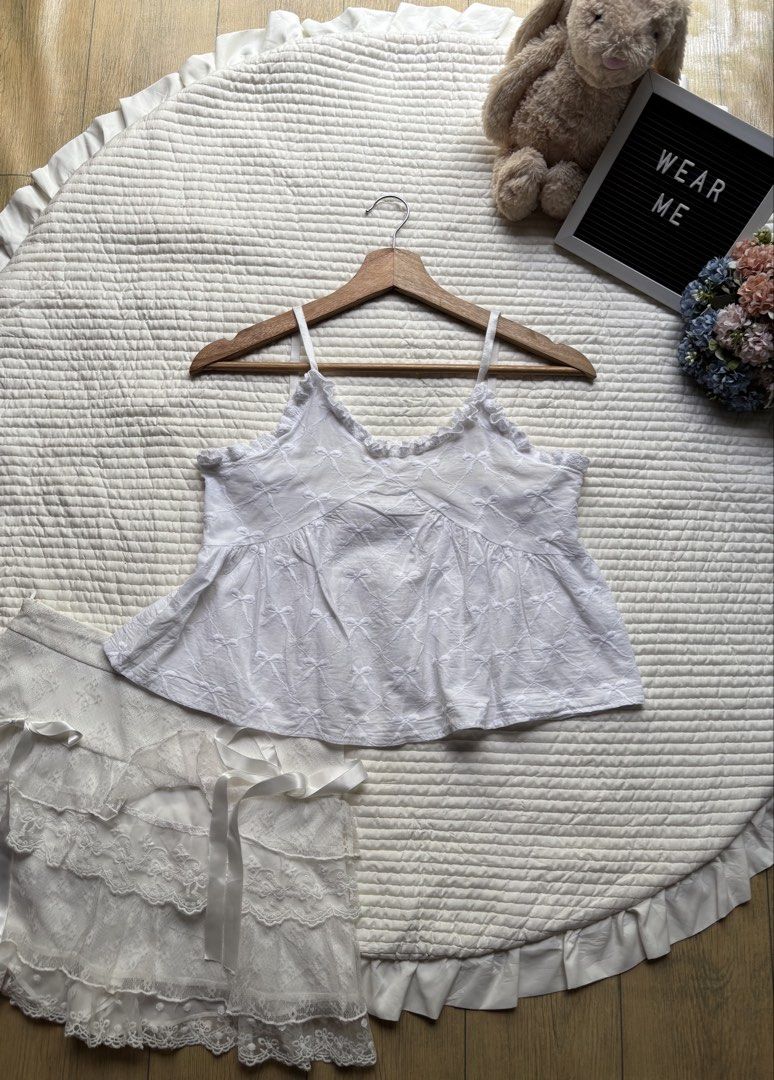 White bow embroidered camisole top ruffled trim (Category: Sleeveless) located in Manila. Submitted by wearme.hh (Listing ID 1469713486, Image 1). Description: - Color: White with allover bow embroidery - Material: Soft, breathable cotton - Features: Delicate ruffled V-neck trim & thin adjustable straps - Fit: Flowy babydoll silhouette - Styling: Great for warm weather or layering under cardigans.