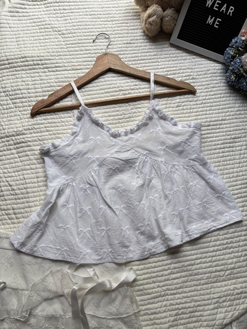 White bow embroidered camisole top ruffled trim (Category: Sleeveless) located in Manila. Submitted by wearme.hh (Listing ID 1469713486, Image 2). Description: - Color: White with allover bow embroidery - Material: Soft, breathable cotton - Features: Delicate ruffled V-neck trim & thin adjustable straps - Fit: Flowy babydoll silhouette - Styling: Great for warm weather or layering under cardigans.