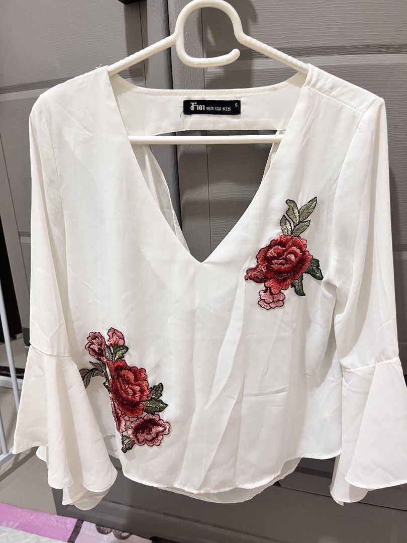 White Floral Embroidered Blouse (Category: Blouses) located in Taguig. Submitted by notyoursam (Listing ID 1469690722, Image 1). Description: - Style: White blouse with red embroidered rose patches on the front and left sleeve - Neckline: Deep V-neck with a cute cutout detail at the back - Sleeves: Long bell sleeves with stylish flared cuffs - Fit: Lightweight, relaxed, and comfy - Size: Tagged Size S.