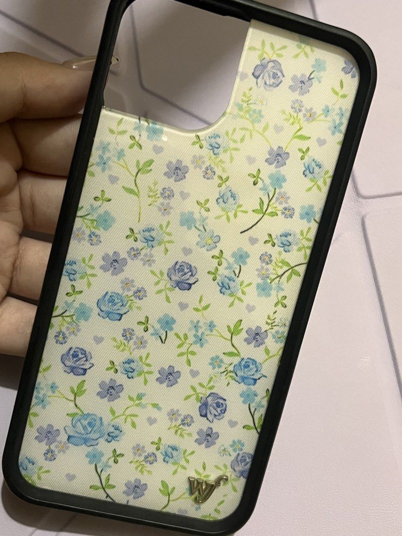 Wildflower Case for Iphone 13/14 (Category: Cases & Sleeves) located in Legazpi City. Submitted by sandras. (Listing ID 1469701629, Image 1). Description: - Brand: Wildflower Cases - Compatibility: Designed for iPhone 13 and iPhone 14 - Design: Aesthetic blue floral print with green vines and tiny heart details - Features: Durable black protective bumper frame and signature metal 'WF' logo - Condition: Excellent, well-maintained.