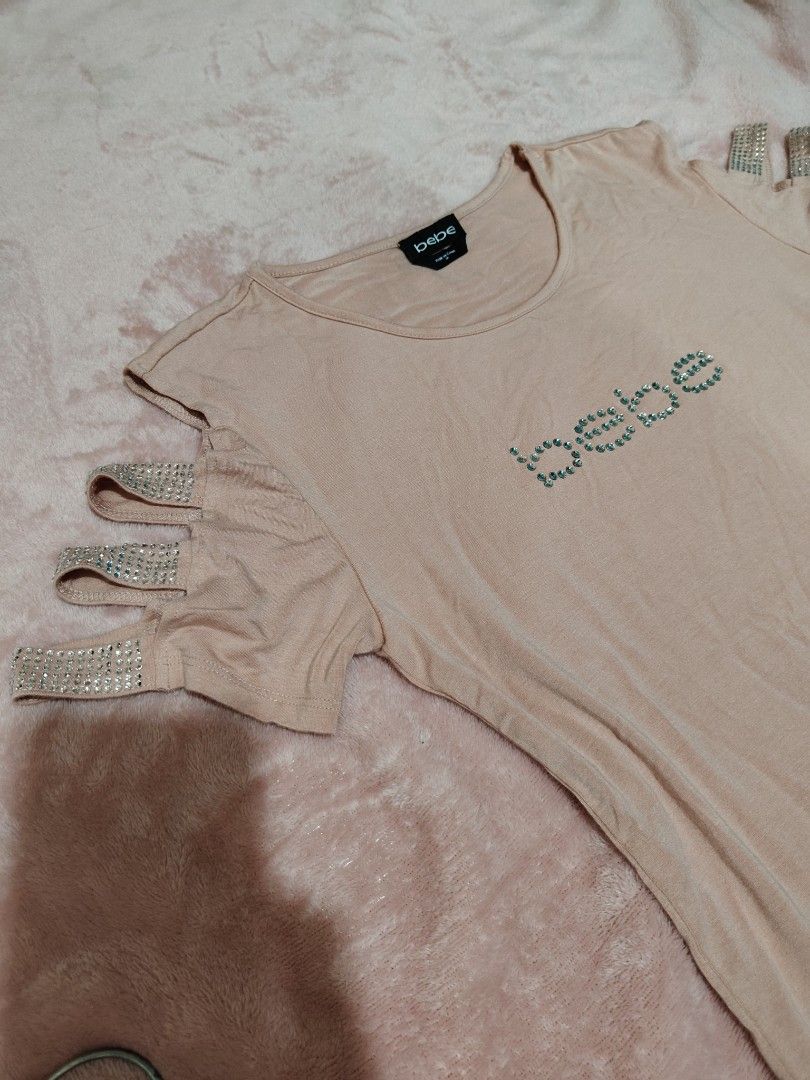 Y2k Bebe Rhinestone Cold Shoulder Top Size M (Category: Sleeveless) located in Villasis. Submitted by trip_thrift15 (Listing ID 1469702656, Image 2). Description: - Brand: Bebe - Color: Pink - Size: Medium - Material: Soft cotton blend - Design: Cold shoulder with rhinestone-accented straps - Detail: Signature Bebe rhinestone logo spelled out on the chest - Neckline: Classic round neckline - Condition: Excellent pre-loved or brand new (ready to w