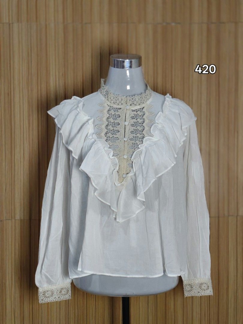 ZARA White Lace Ruffle Blouse Top (Category: Blouses) located in Taguig. Submitted by ashie_clothing (Listing ID 1469687028, Image 2). Description: - Brand: Zara - Color: White with beige lace accents - Condition: Brand new with tag attached - Features: Ruffle trim front, high neckline with crochet lace edging - Sleeves: Long sleeves with matching lace cuffs - Closure: Covered button placket.