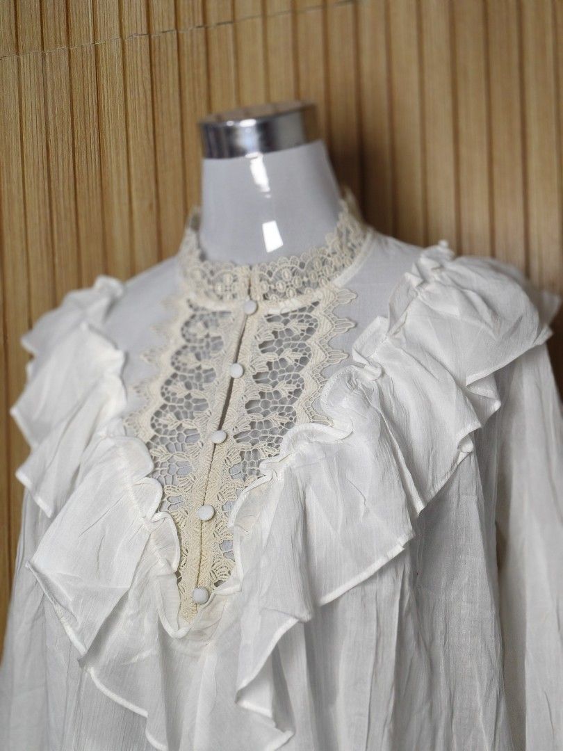 ZARA White Lace Ruffle Blouse Top (Category: Blouses) located in Taguig. Submitted by ashie_clothing (Listing ID 1469687028, Image 3). Description: - Brand: Zara - Color: White with beige lace accents - Condition: Brand new with tag attached - Features: Ruffle trim front, high neckline with crochet lace edging - Sleeves: Long sleeves with matching lace cuffs - Closure: Covered button placket.